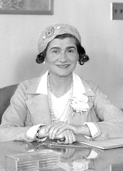 Coco Chanel 1931 年在办公桌前的肖像照片，佩戴软帽与珍珠项链