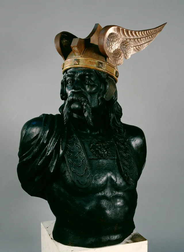 A bronze bust of a bearded man in a winged helmet with a copper band, on a pale plinth