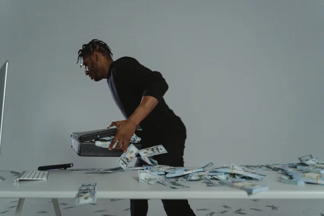 Person gathering stacks of cash into a briefcase with urgency
