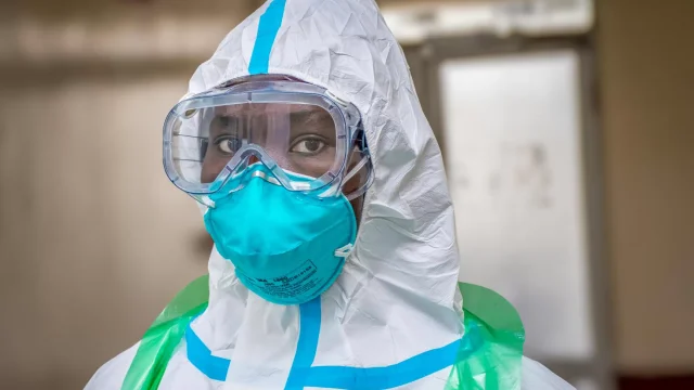 A health worker in a white protective suit, goggles and a blue respirator, with only the eyes visible
