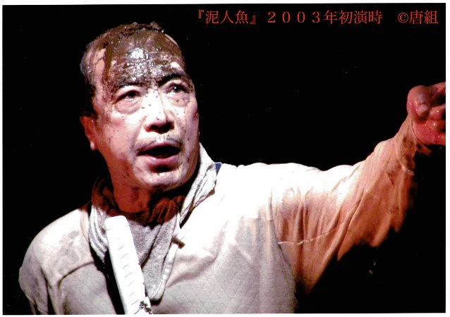 舞台上一位满身泥浆的男子伸出手臂,背景漆黑