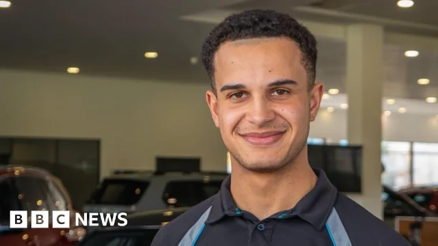 Tyrell Cambridge stands in a vehicle showroom wearing a dark work polo shirt.