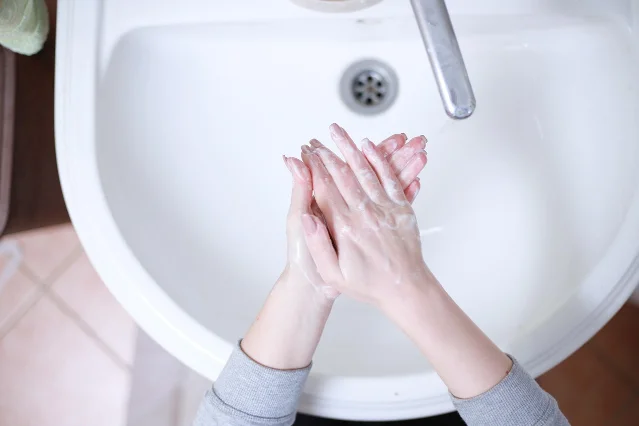 Two soapy hands rubbing together above a white bathroom basin