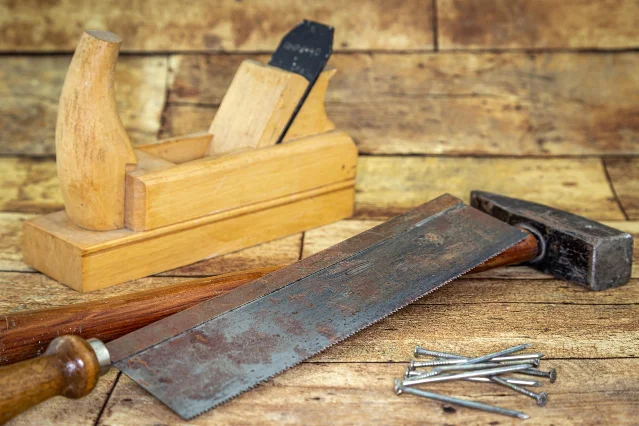 A wooden hand plane, a hammer and a saw blade with surface rust on a workbench