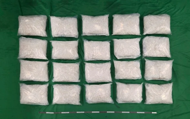 25 clear plastic evidence bags of suspected ketamine arranged in five rows on a green examination cloth, with a ruler for scale below them