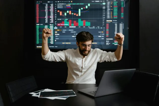 Excited trader at desk with stock chart screen