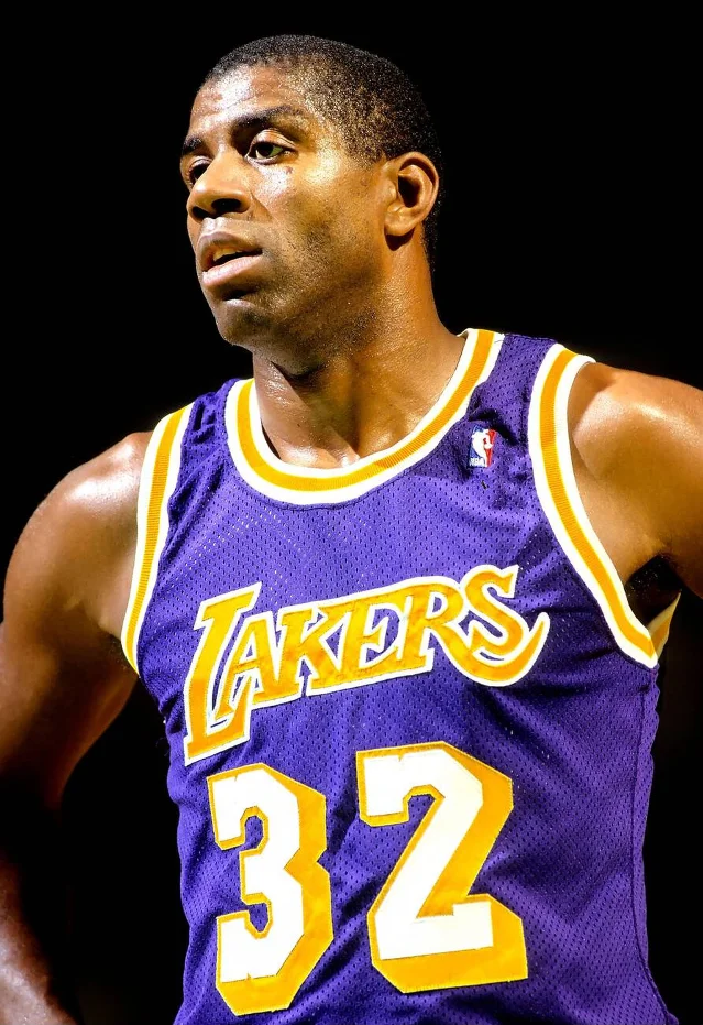 A basketball player in a purple Lakers jersey turning toward the camera against a black background