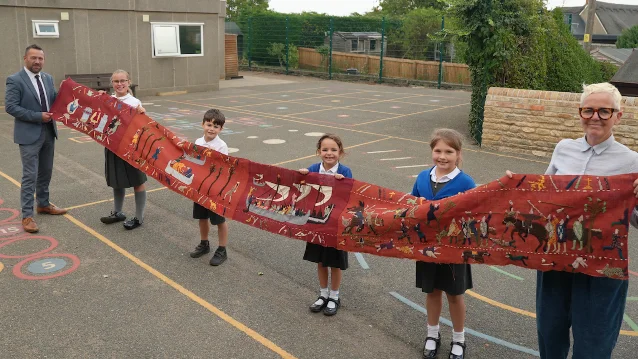 Children and adults holding a long embroidered tapestry across a playground