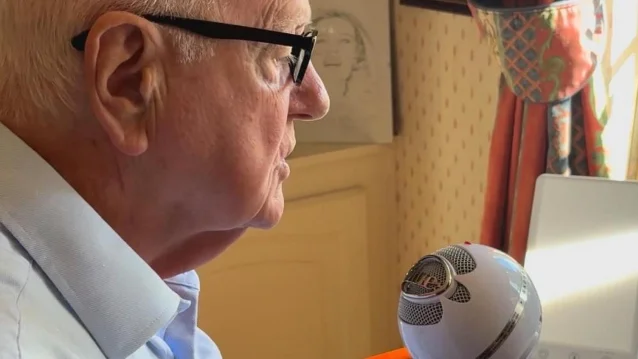 A man in glasses seen in profile at a desk, looking towards a white spherical smart speaker