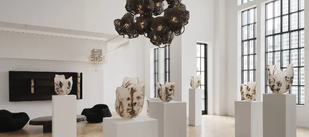 A bright gallery with translucent sculptural vessels containing pressed flowers and plant fragments on white plinths
