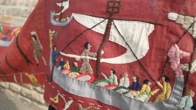 Close view of hand-stitched figures in a boat on a red ground