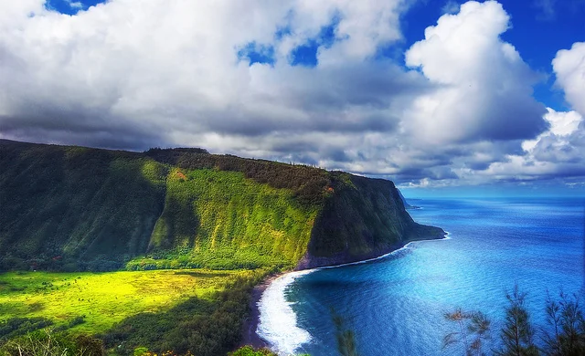 Waipo Valley coastal cliffs on the Big Island with white sand beach, blue water, and cloud-streaked sky