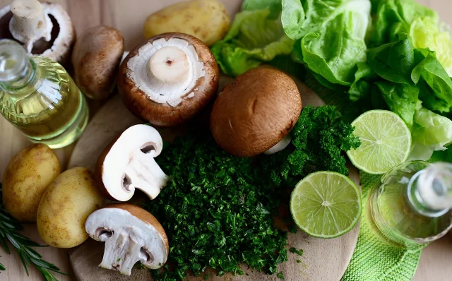 Mushrooms, potatoes, greens, herbs, and lime grouped on a cutting board