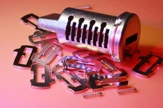 Disassembled lock cylinder and metal components — similar to the hardware inside a window espagnolette assembly