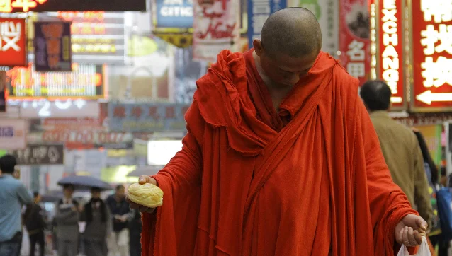 一位红袍僧人低头走在霓虹招牌密集的街道上