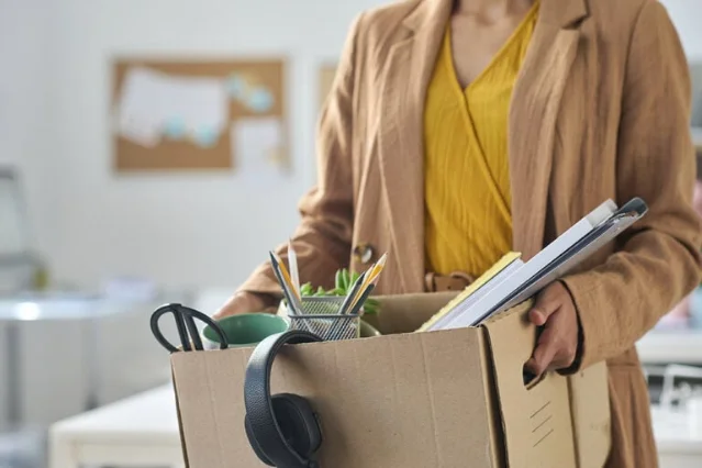 Woman leaving an office carrying a box of belongings after a layoff