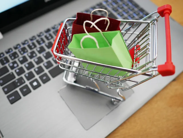 A shopping cart with paper bags beside a laptop