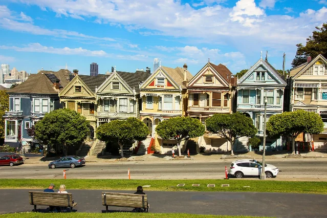 Colorful Victorian row houses in San Francisco's Alamo Square neighborhood with downtown skyline behind