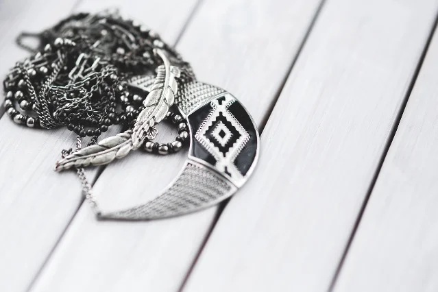 Silver chains and a pendant necklace lying on a pale wooden surface