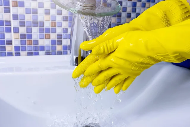 Two hands in yellow rubber gloves held under a running tap