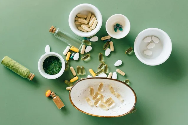 Top view of herbal and pharmaceutical supplements in ceramic bowls on a green background