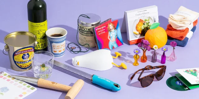 Various gift items including a vinyl record, plush toy, candles, and a tin of mustard arranged on a light background