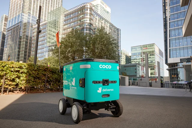 印有 COCO 与 deliveroo 标识的配送机器人停在伦敦写字楼前