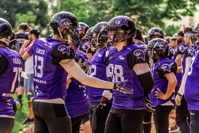 Football players gather on the sideline between plays, reflecting the pre-camp strategy window when ADP shifts are most consequential