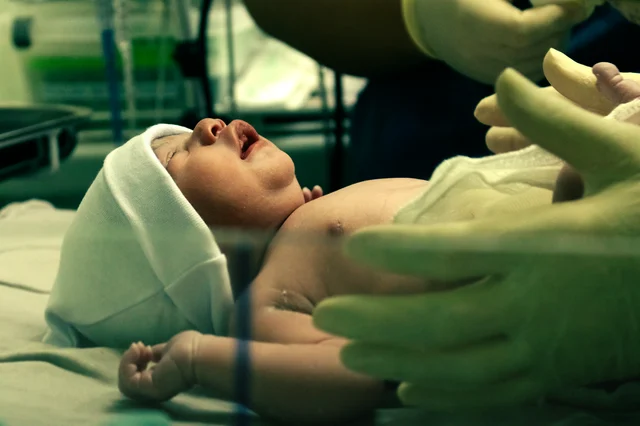 A newborn being gently handled by a gloved nurse in a hospital setting