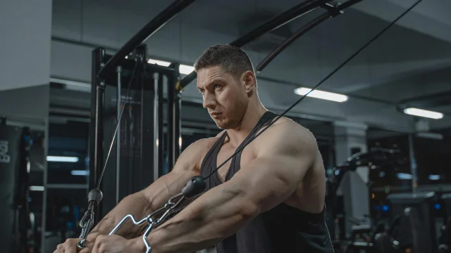 Muscular man exercising on a cable machine in a modern gym setting