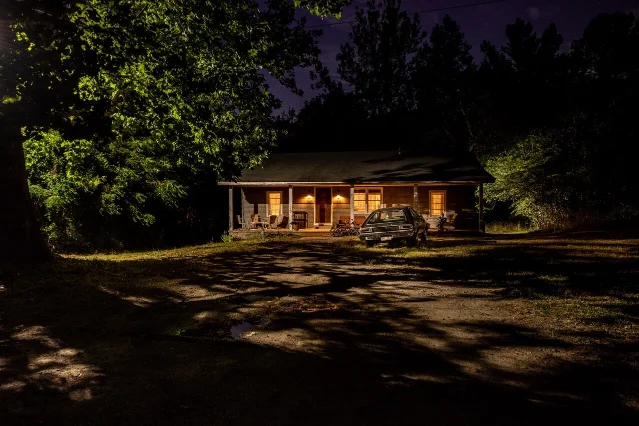 The Byers House at night, porch lights lit, with a hatchback parked on the drive