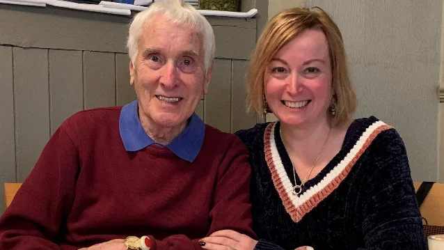 John Richardson, an older man in a burgundy sweater, seated beside his daughter Kate Davis