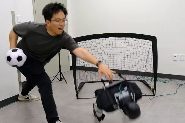 一名研究者伸手去接一台正在向后倒下的白色双足机器人
