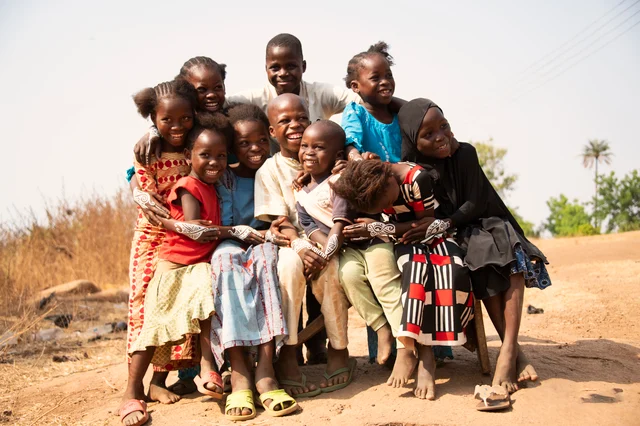 A group of Nigerian children sitting together outdoors, smiling and wearing colorful clothes with white body art