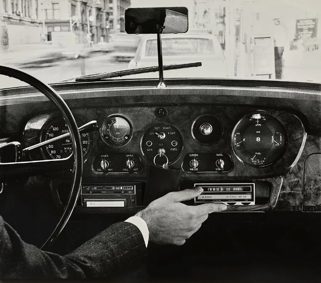A hand turning the tuning knob on a vintage car dashboard radio