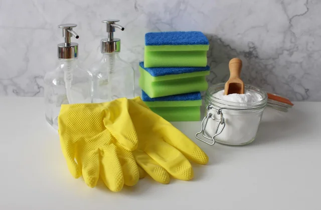 Yellow gloves, sponges, spray bottles, and a jar of baking soda on a counter