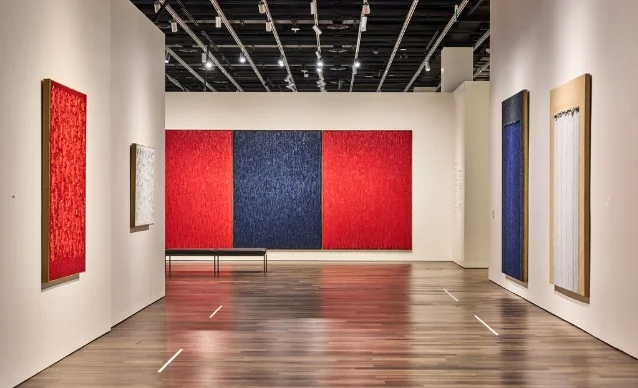 白色展厅里,正面是一组红底与蓝底相接的多联画,两侧挂着红色与蓝色的单幅作品