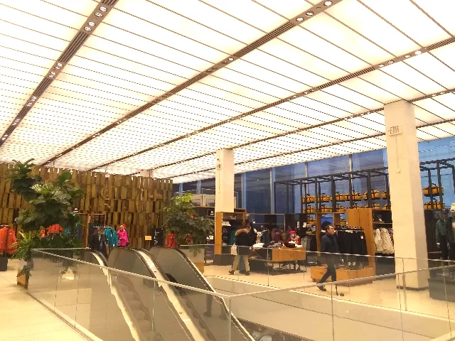 A luminous second-floor retail interior with ceiling grid, escalator, and glass facade