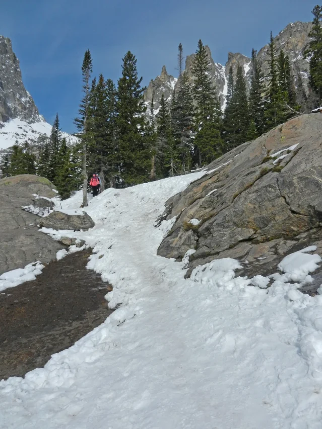 NPS photo from May 21, 2026: a hiker in traction devices picks a line through the icy, snow-packed steep section between Dream Lake and Emerald Lake