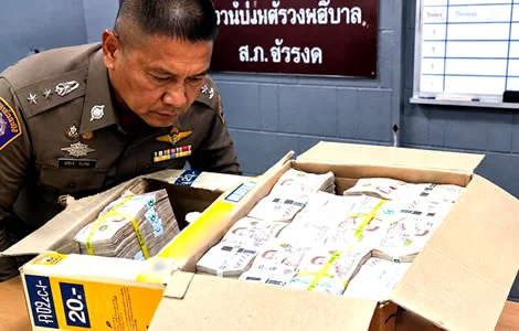 Thai officers inspecting bundles of 1,000-baht notes inside opened snack boxes