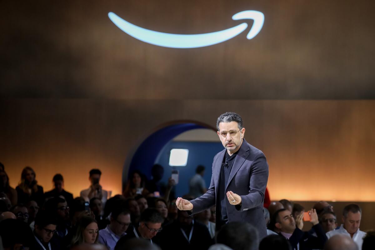 Panos Panay speaking at an Amazon event with illuminated Amazon smile logo behind him