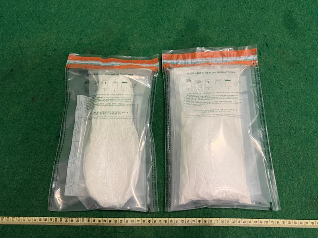 Two tamper-evident evidence bags each containing white powder laid flat on a green examination surface, ruler visible at bottom — approximately 10 kg ketamine from the Amsterdam-route seizure