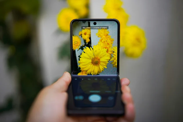 A sleek foldable phone photographed mid-fold, sharp against a bokeh background of yellow flowers