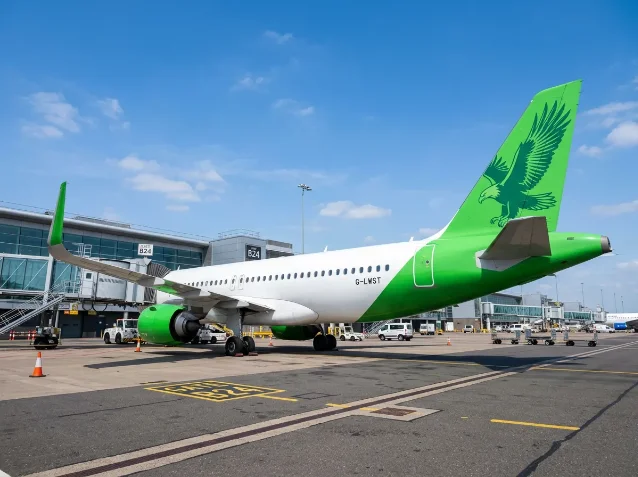 Green and white narrow-body aircraft with eagle tail livery parked at airport gate, clear blue sky