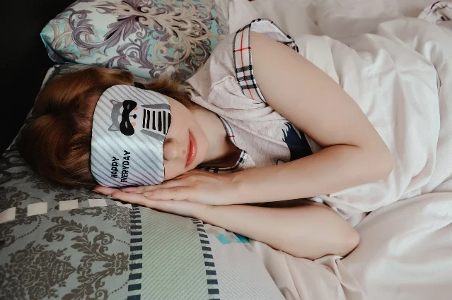 Person wearing a sleep mask in bed — representing sleep health interventions
