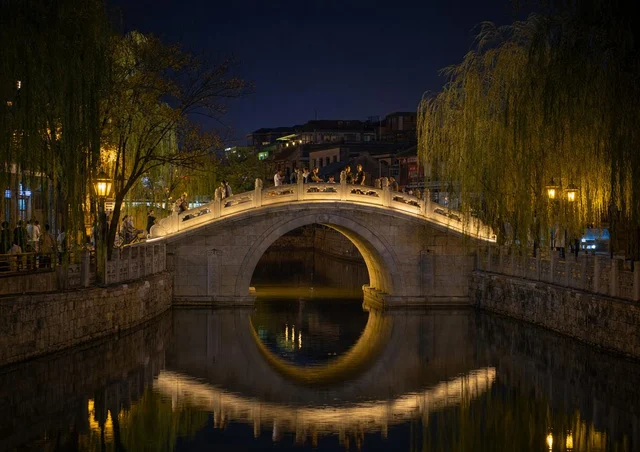 什刹海银锭桥夜景,单孔石拱桥倒影水面,两岸灯光柔和
