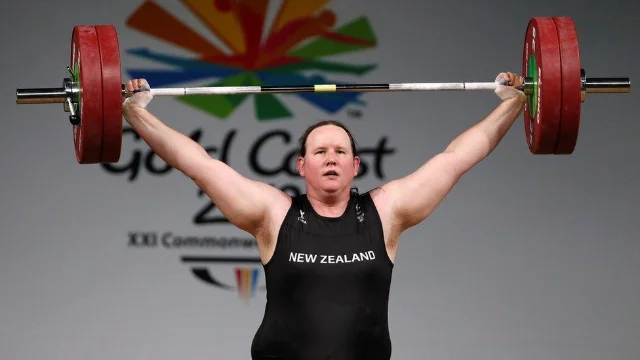 Laurel Hubbard lifts the barbell overhead at the 2018 Commonwealth Games in Gold Coast, NEW ZEALAND across her singlet, the Commonwealth Games logo on the backdrop behind her