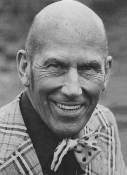 Ted Tinling photographed in 1975, bald, smiling, in a plaid jacket with a polka-dot pocket square