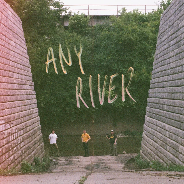 Styrofoam Winos Any River album cover: three band members standing in a concrete drainage channel, green foliage, handwritten-style yellow lettering