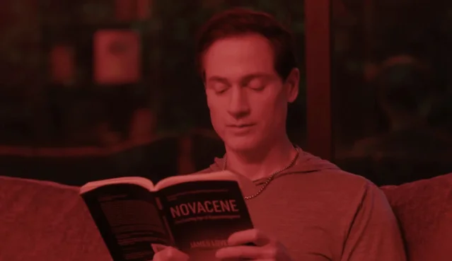 Bryan Johnson reading a book under red/amber lighting during his evening wind-down routine